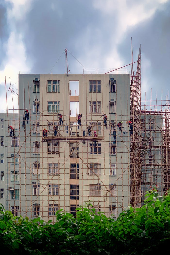 Tall building under construction with workers on scaffolding against a cloudy sky.