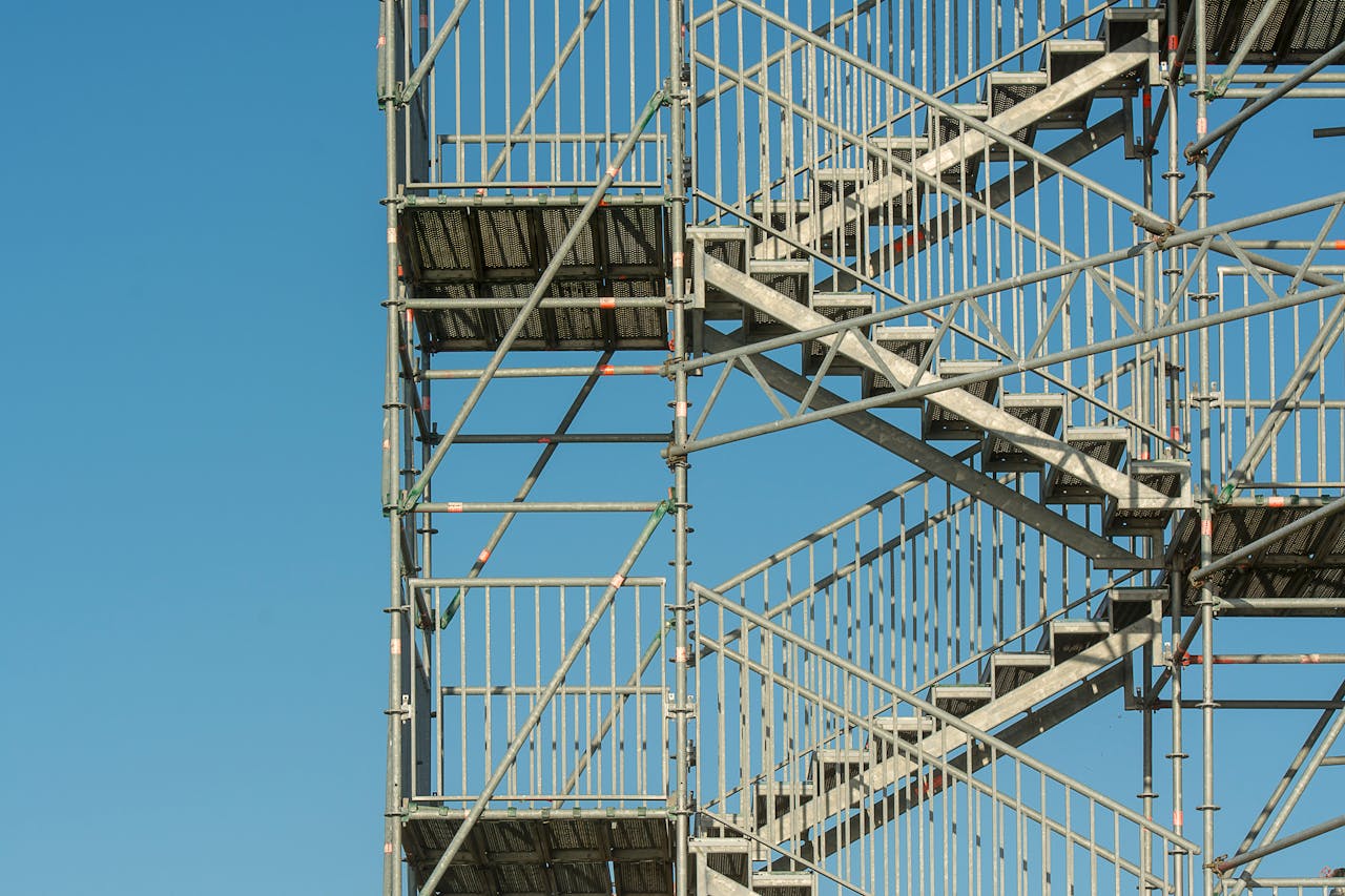 Close-up of metal scaffolding structure with stairs against a clear blue sky, illustrating construction and industrial themes.